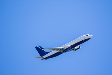 flying white and blue new passenger airplane against blue sky.  airplane without logo with copy...