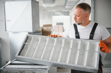 A male worker holds an air filter for air conditioning in an office space. Installation of an air...