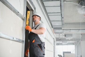 Man holding level against plasterboard, interior drywall. Attic renovation