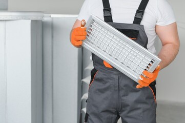 A male worker holds an air filter for air conditioning in an office space. Installation of an air...