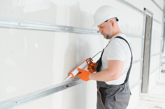 The builder fills the seam between plasterboard plates a silicone gun