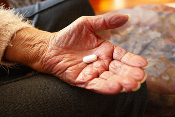 Big white pill in the hand of an elderly woman