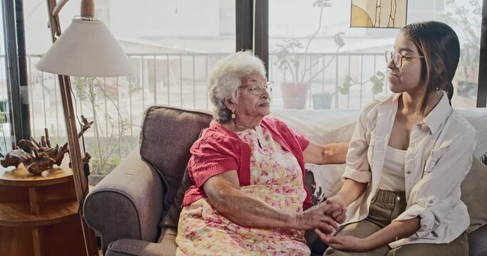 Grandmother and granddaughter sitting on the sofa at home, having a good talk, grandmother and granddaughter enjoying the moment together holding hands.