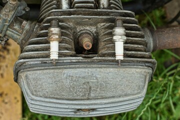  two old used dirty iron ceramic spark plugs for a motorcycle lie on a closed engine in the street at daytime