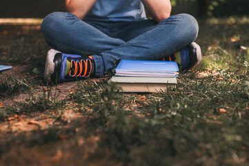 Close-up books laid out on the grass over a teen boy sitting lonely in the park. Back to school and education concept