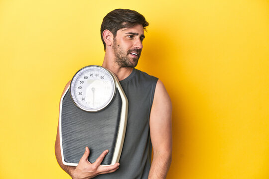 Athletic man with scale, on a yellow studio backdrop looks aside smiling, cheerful and pleasant.