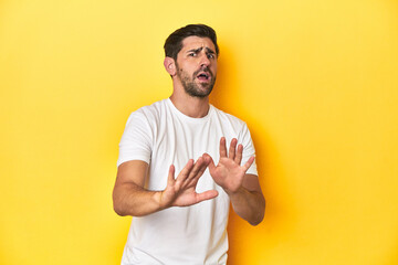 Caucasian man in white t-shirt on yellow studio background rejecting someone showing a gesture of...