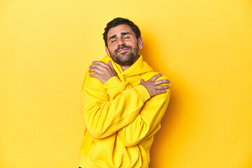 Obraz premium Man in yellow hoodie, monochrome studio backdrop hugs, smiling carefree and happy.