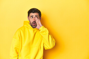 Man in yellow hoodie, monochrome studio backdrop is saying a secret hot braking news and looking aside