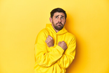 Man in yellow hoodie, monochrome studio backdrop scared and afraid.