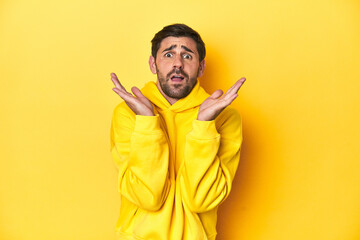 Man in yellow hoodie, monochrome studio backdrop surprised and shocked.