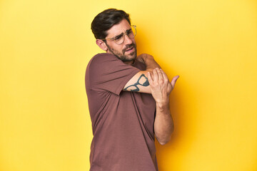 Man stretching arm on a yellow studio background. - obrazy, fototapety, plakaty