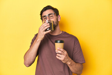 Man letting gourmet coffee beans fall from his hand on yellow studio background.