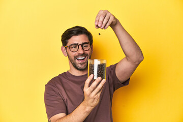 Man letting gourmet coffee beans fall from his hand on yellow studio background.