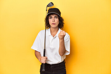 Athletic Caucasian woman with curly hair golfing in studio showing fist to camera, aggressive facial expression.