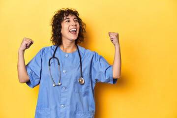 Curly-haired Caucasian woman nurse on yellow studio raising fist after a victory, winner concept.