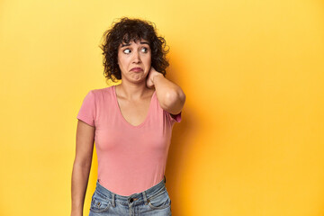 Curly-haired Caucasian woman in pink t-shirt touching back of head, thinking and making a choice.