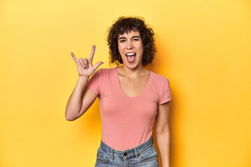 Curly-haired Caucasian woman in pink t-shirt showing a horns gesture as a revolution concept.