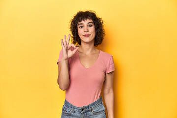 Curly-haired Caucasian woman in pink t-shirt cheerful and confident showing ok gesture.