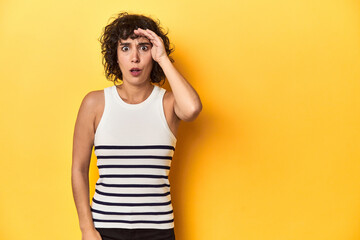 Caucasian curly-haired woman in white tank-top shouts loud, keeps eyes opened and hands tense.