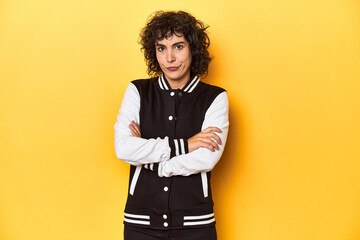 Curly-haired Caucasian woman in baseball jacket suspicious, uncertain, examining you.