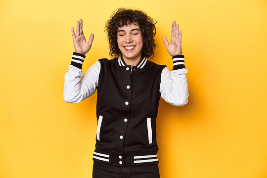 Curly-haired Caucasian woman in baseball jacket joyful laughing a lot. Happiness concept.