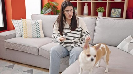 Young hispanic woman with chihuahua dog using stick roll to clean pet hair at home