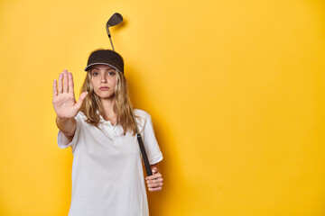 Young Caucasian golfer with cap and golf club on yellow backdrop, standing with outstretched hand...