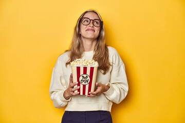 Young Caucasian holding popcorn, cinema concept on yellow backdrop, dreaming of achieving goals and...
