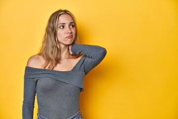 Elegant blonde on yellow backdrop, touching back of head, thinking and making a choice.
