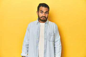 Casual young Latino man against a vibrant yellow studio background, sad, serious face, feeling miserable and displeased.