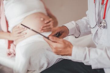 Naklejka premium Concept Motherhood and Pregnant, Prenatal care and pregnancy. Male doctor checkup list the baby ultrasound picture on tablet to pregnant woman sitting on the bed.