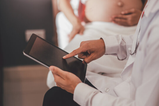 Concept Motherhood and Pregnant, Prenatal care and pregnancy. Male doctor checkup list the baby ultrasound picture on tablet to pregnant woman sitting on the bed.
