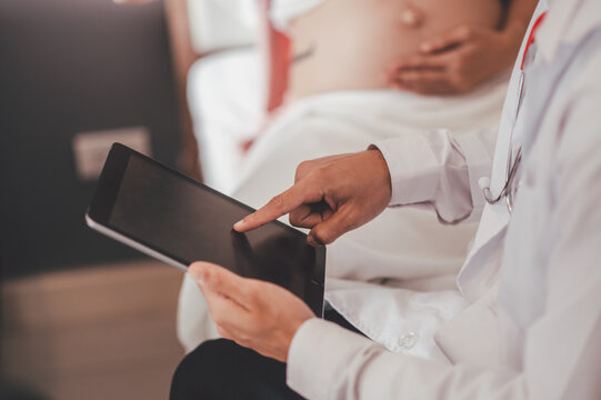 Concept Motherhood and Pregnant, Prenatal care and pregnancy. Male doctor checkup list the baby ultrasound picture on tablet to pregnant woman sitting on the bed.