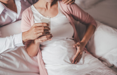 Concept Maternity and Pregnant, Prenatal care and pregnancy. Portrait of Pregnant woman sitting on a white bed Her husband holds a glass of milk and sends her fresh milk in a clear glass for her to dr