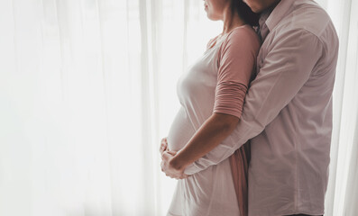 Concept Maternity and Pregnant, Prenatal care and pregnancy. Love of family, motherhood. Pregnant woman and her husband with big belly standing hug side windows at home.