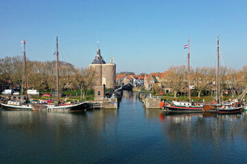 Drone photo of the old lock in Enkhuizen with the drommedaris tower in the background and a wooden sailing boats in the front.