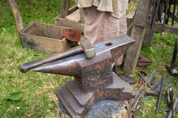 Blacksmith's anvil with hammer in the background with metal tools