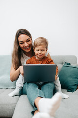 Fototapeta premium Happy middle age woman playing with her little son at home. They are using smart phone and laptop computer for playing, learning and online surfing.