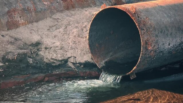 A large rusty pipe from which polluted industrial water flows. Environmental problem of water pollution.