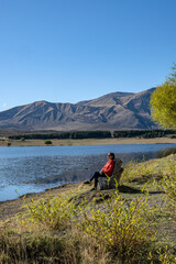 Senior woman rests sitting sunbathing in front of Laguna Zeta, in Esquel, Chubut Argentina.