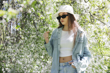 Beautiful teen girl with long blond hair and a hat in a spring park.