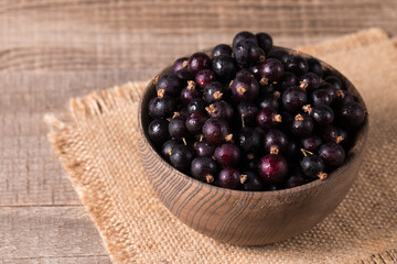 Black currant in a bowl on wooden background. Organic berries. 