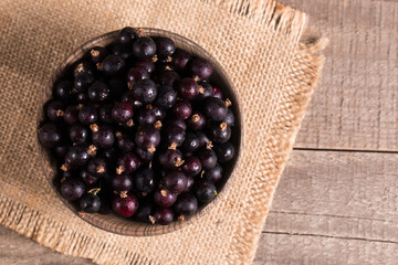 Black currant in a bowl on wooden background. Organic berries. 