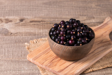 Black currant in a bowl on wooden background. Organic berries. 