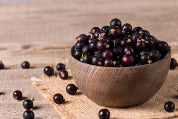 Black currant in a bowl on wooden background. Organic berries. 