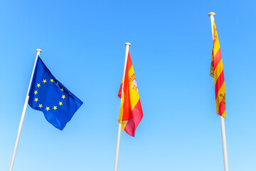 EU flag Spanish flag local Ibiza flag waving in the wind on blue sky background