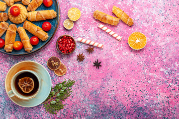 Fototapeta na wymiar top view sweet delicious bagels inside tray with plums and cup of tea on pink desk pastry cake biscuit cookie sweet sugar