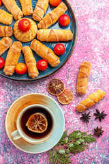 top view sweet delicious bagels inside tray with plums and tea on pink desk pastry cake biscuit cookies sweet sugar