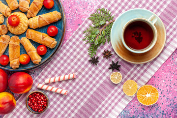 top view sweet delicious bagels inside tray with plums fresh peaches and cup of tea on light-pink desk cake biscuit cookies sweet sugar pie